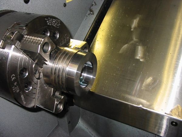 Close-up of a metal lathe chuck holding a cylindrical metal workpiece.