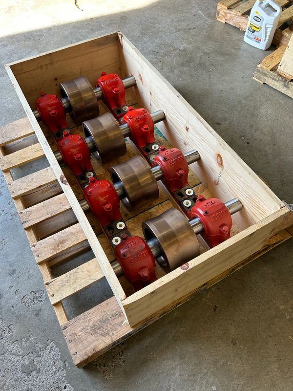 Metal rollers with red bearings packed in a wooden crate on a pallet.