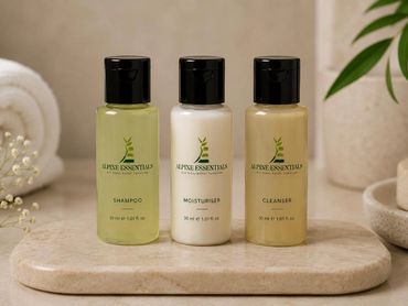 Three Alpine Essentials skincare bottles on a stone tray in a bathroom.