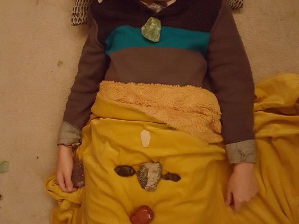 Person lying down with stones arranged on their body under a yellow blanket.