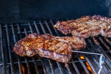 Juicy steaks grilling over an open flame on a barbecue.