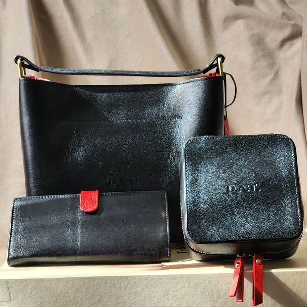 Set of black leather accessories with red accents, including a handbag, wallet, and case.
