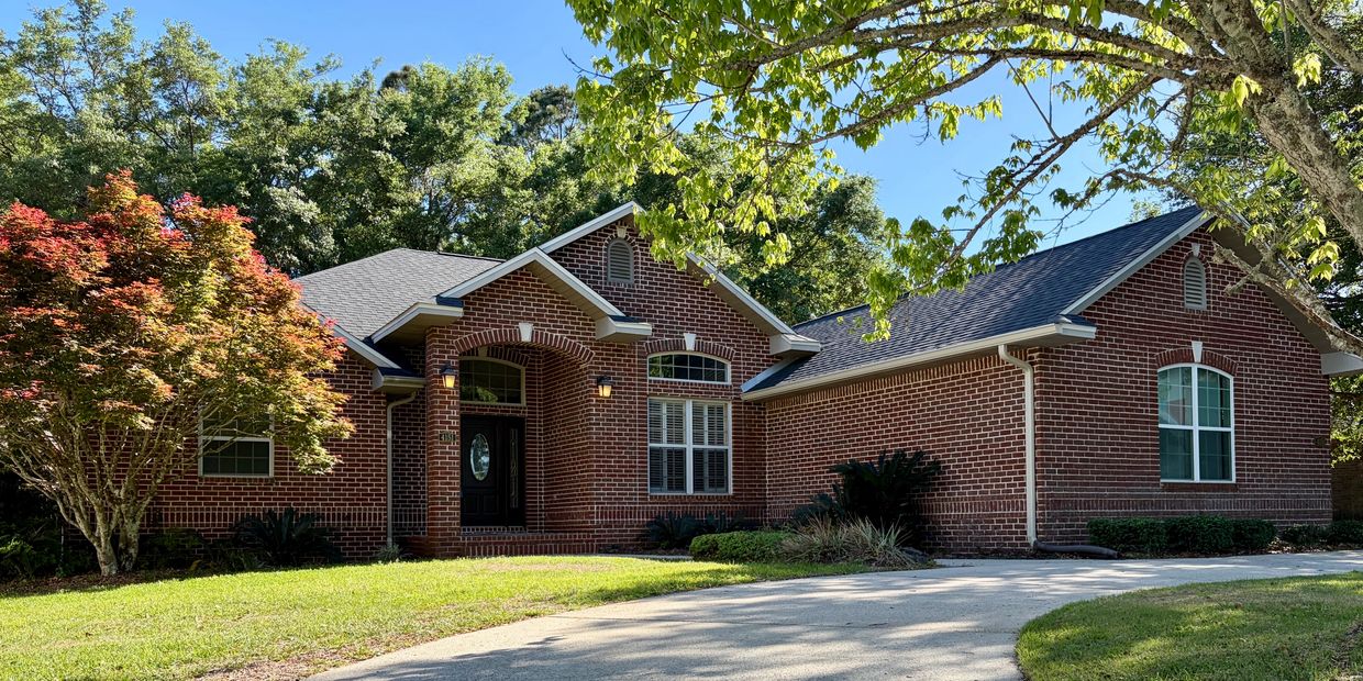 Front view of 4151 Castle Gate Dr, a single-story brick home with a circular driveway, mature trees,