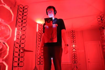 Person wearing headphones in a red-lit room holding a device.