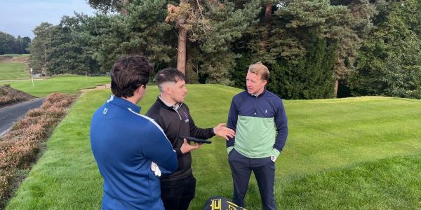 Tres hombres conversan en un campo de golf.