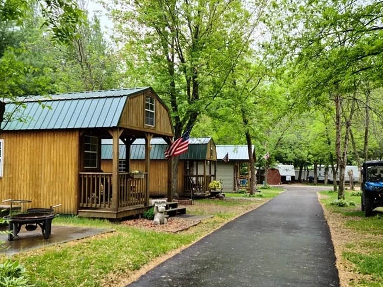 Three cabins on the left of blacktop drive and surrounded by trees.