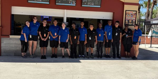 Group of employees standing outside a BBQ food stand under clear blue sky.