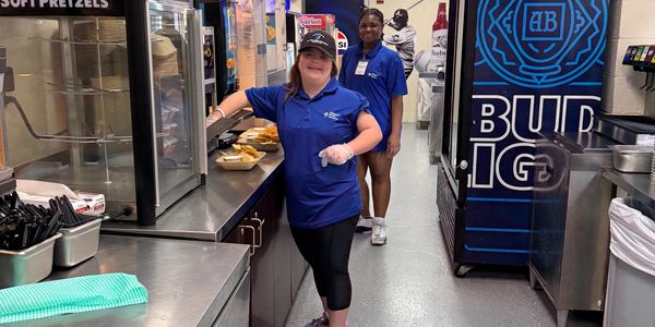 Two women in blue uniforms working in a concession stand.