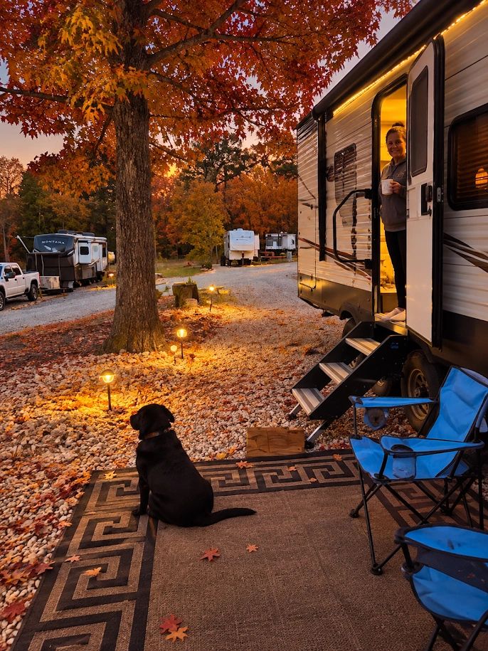 A black dog and a woman outside a trailer in autumn.