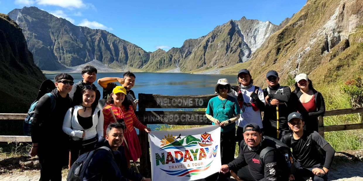 Group photo of hikers at Pinatubo Crater with a scenic mountain lake background.