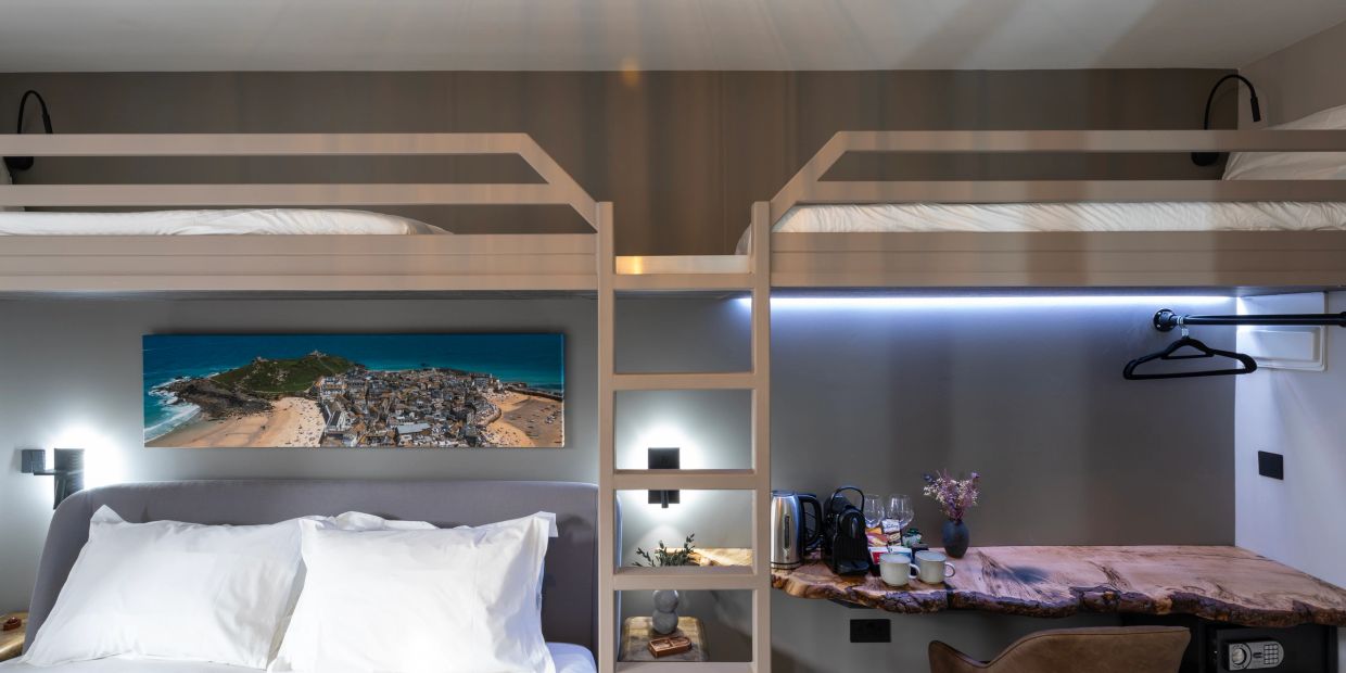 Modern bunk bed above a bed with a wooden desk beneath and wall art.