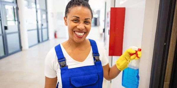 Smiling cleaner in blue overalls with a spray bottle.