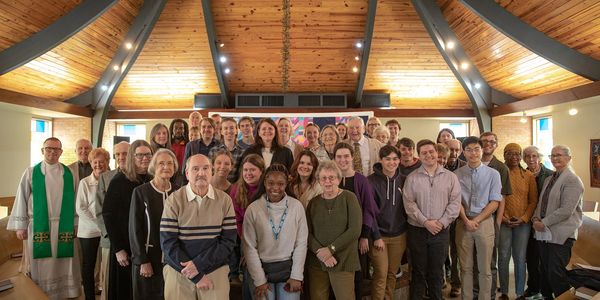 A diverse group of people gathered inside a church with wooden ceiling beams.