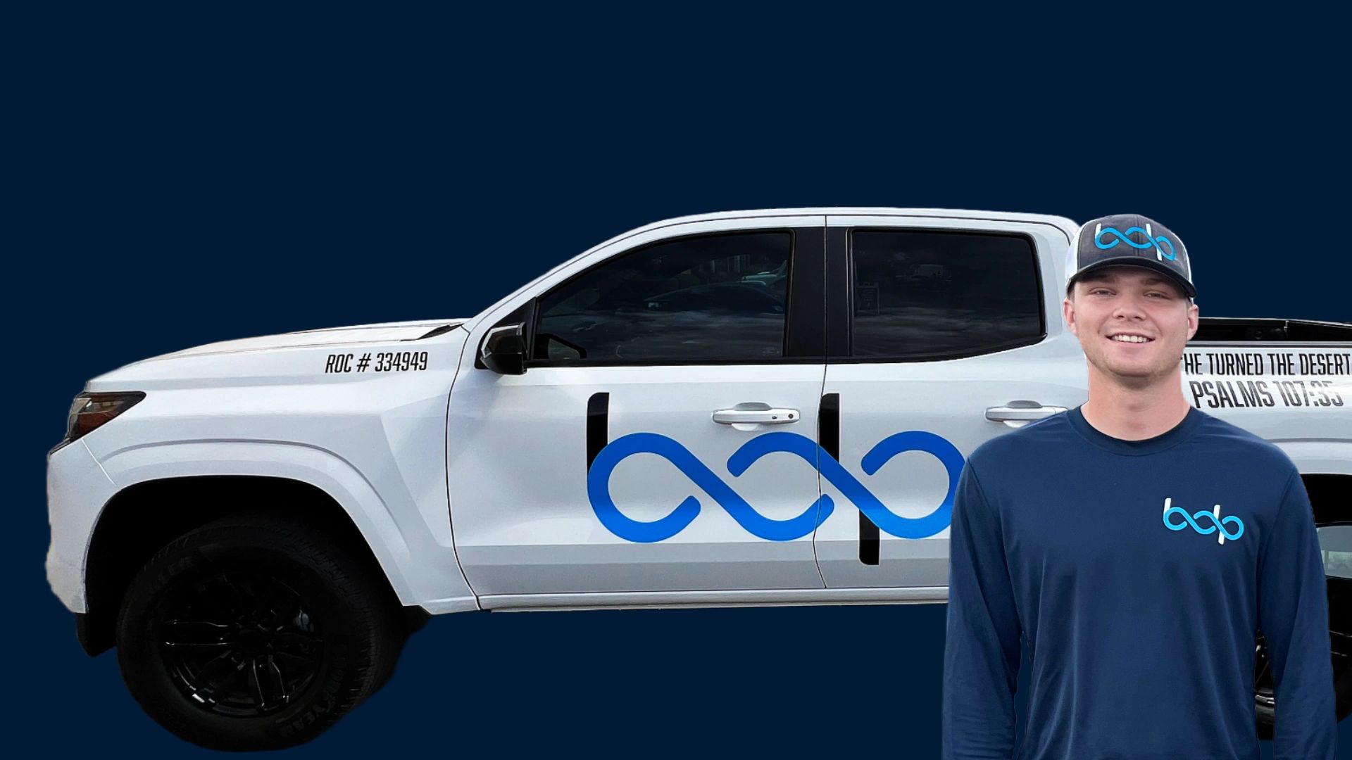 Man standing next to a white truck with blue logo and text on a dark background.