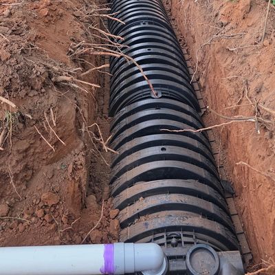 Large black drainage pipe laid in a trench surrounded by dirt and trees.