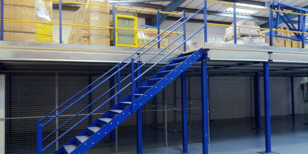 Blue metal staircase leading to a storage mezzanine with packed boxes.