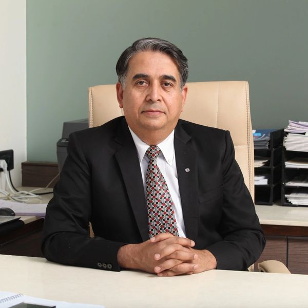 Confident man in suit sitting at an office desk with hands clasped.