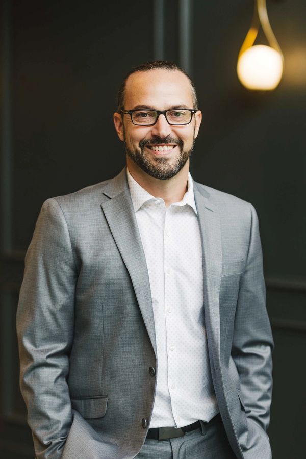 Smiling man in a gray suit and glasses.