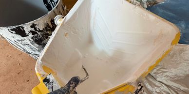 A paint tray with white paint and a roller inside, next to a paint bucket.