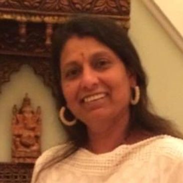 Woman smiling, wearing white clothes and large earrings.