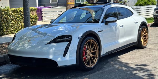 White Porsche Taycan Cross Turismo with bronze wheels parked on a sunny street.