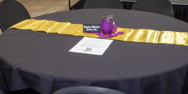 Table set with black tablecloth, gold runner, and purple candle centerpiece.