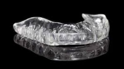 Clear dental night guard with reflection on black surface.