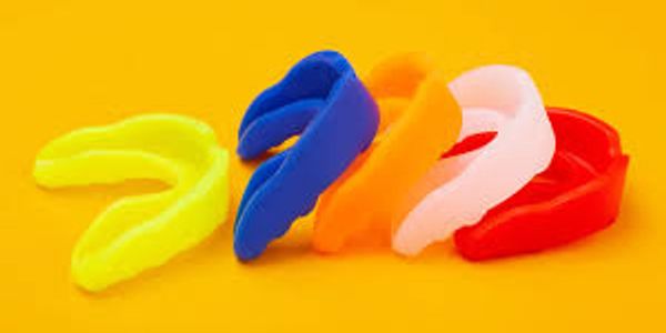 Five colorful mouthguards arranged on a yellow surface.