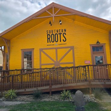 Bright yellow building of Southern Roots Brewing Company with wooden ramp.