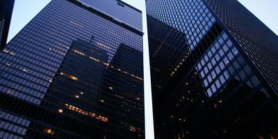 Two tall glass skyscrapers reflecting city lights at dusk.