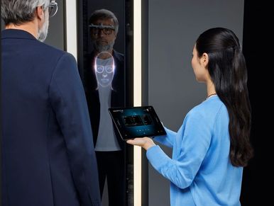 A woman uses a tablet for facial recognition on a man in front of a smart mirror.