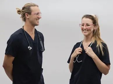 Two smiling healthcare professionals in black scrubs with stethoscopes.