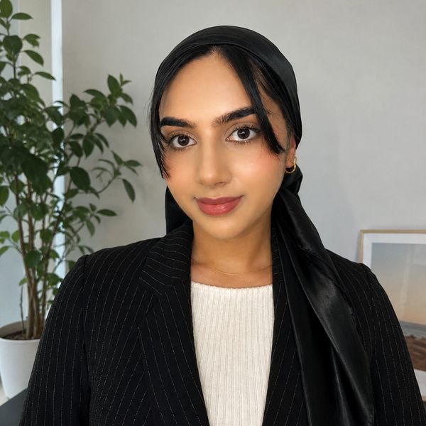 A woman wearing a black headscarf and pinstripe blazer, smiling gently.