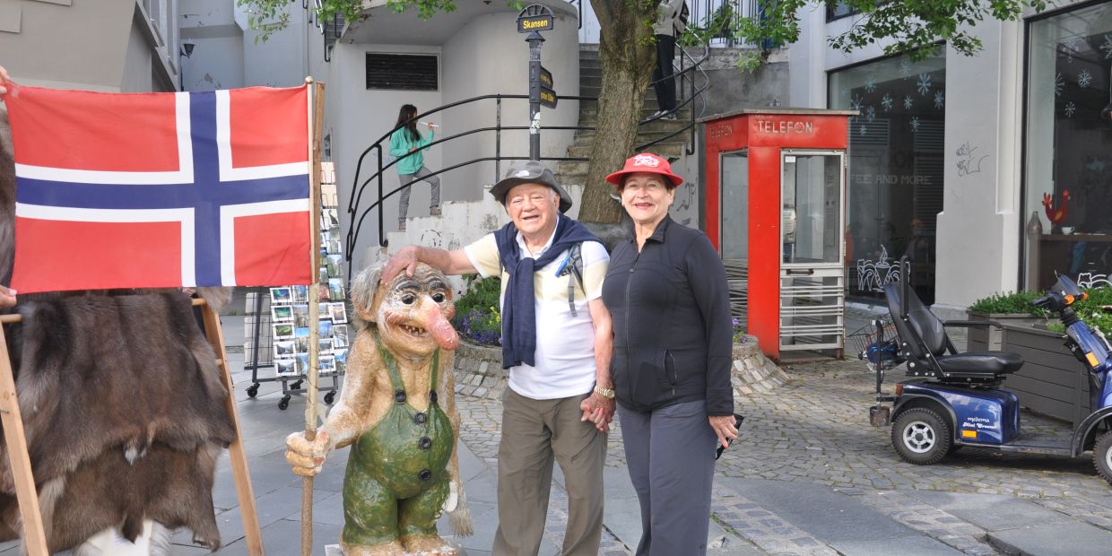 Elderly couple posing with a troll statue and Norwegian flag.