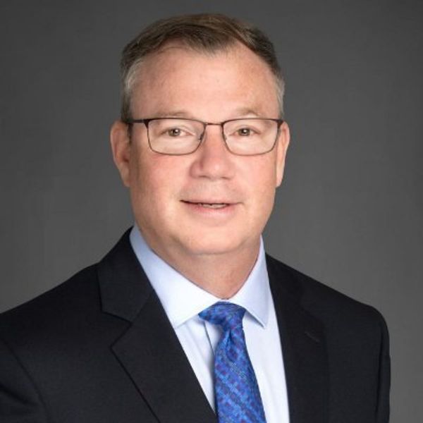 Professional headshot of a middle-aged man wearing glasses and a suit.