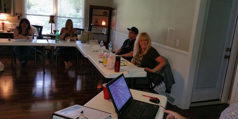 People gathered around tables in a cozy room with laptops and notebooks.