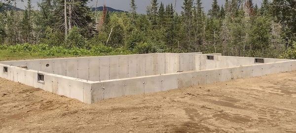 Freshly poured concrete foundation set against a scenic forested backdrop in Northern NH.