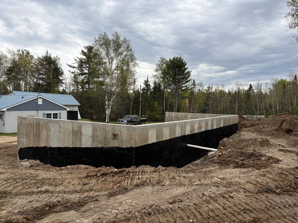 A poured concrete foundation with applied waterproofing and visible drainage piping.