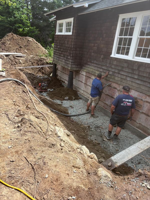 Workers performing foundation repair and compaction along the side of a home by Swallow and Sons