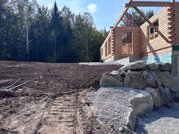 Completed grading and boulder retaining wall installation at an in-progress log home build. Durable.
