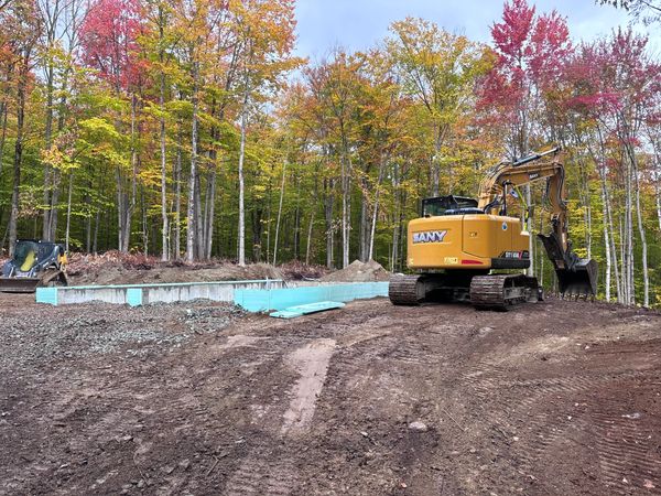 Heavy equipment on-site completing excavation and backfilling around a poured concrete foundation, s