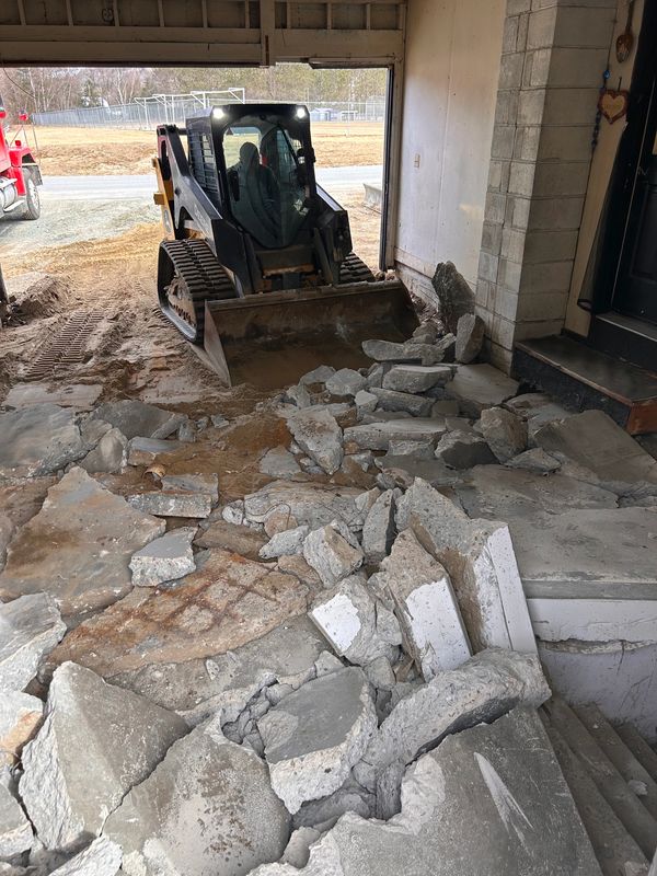 Skid steer clearing debris from a broken concrete floor during garage reconstruction. Efficient.