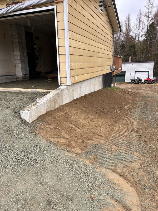 A clean, finished gravel ramp and soil slope lead up to a garage foundation. .