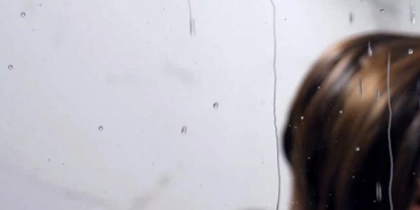 Raindrops on a window with a blurred person behind the glass.