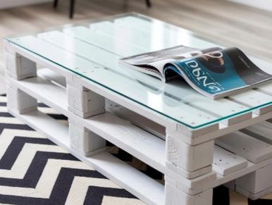 A glass-top coffee table made from painted wooden pallets on a chevron rug.