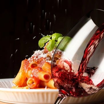 Red wine being poured into a glass with rigatoni and red sauce Italian dish behind