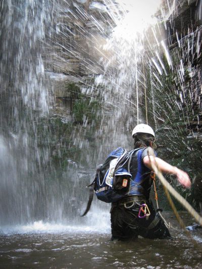 A man adjusting climbing ropes at the base of a waterfall