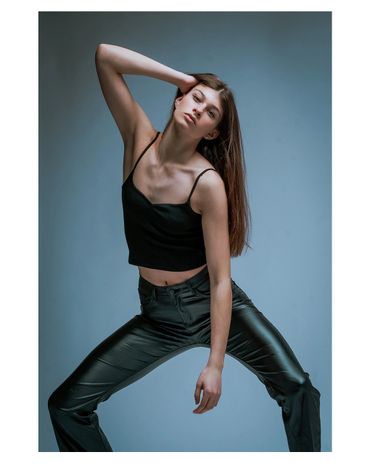 Young woman posing confidently in black top and leather pants.