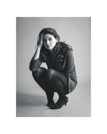 Black and white photo of a woman squatting thoughtfully.
