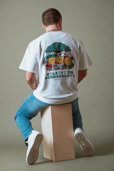 Man wearing a white T-shirt with smiley faces and text sitting on a wooden block.